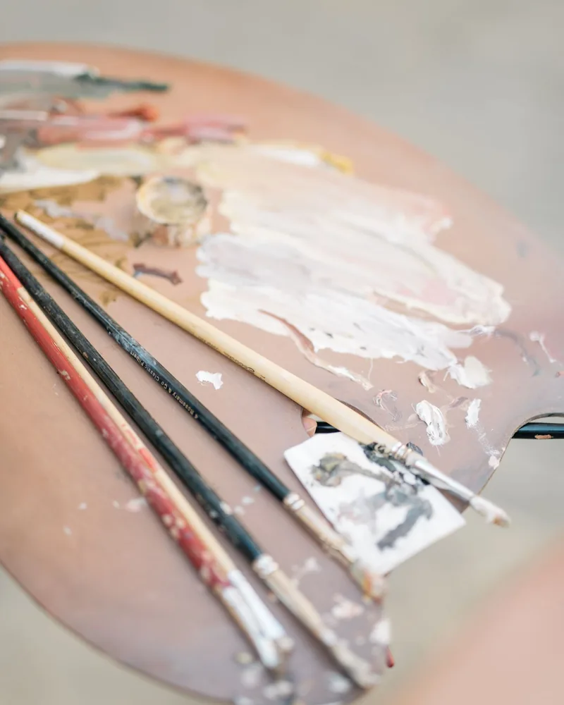 Paleta de madera con mezclas de pintura y varios pinceles apoyados encima